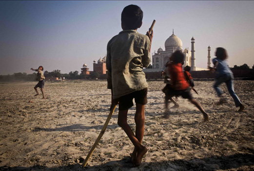 Près du Taj Mahal, en Inde, un enfant victime de la poliomyélite, appuyé sur sa canne, regarde ses amis jouer au ballon